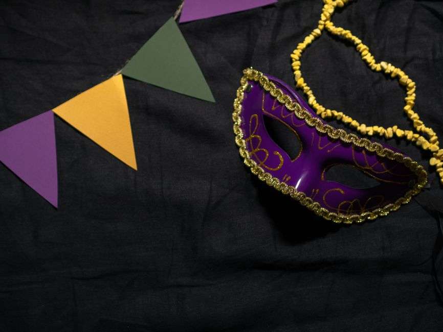 A purple Mardi Gras mask decorated with beads, evoking Carnival season celebrations
