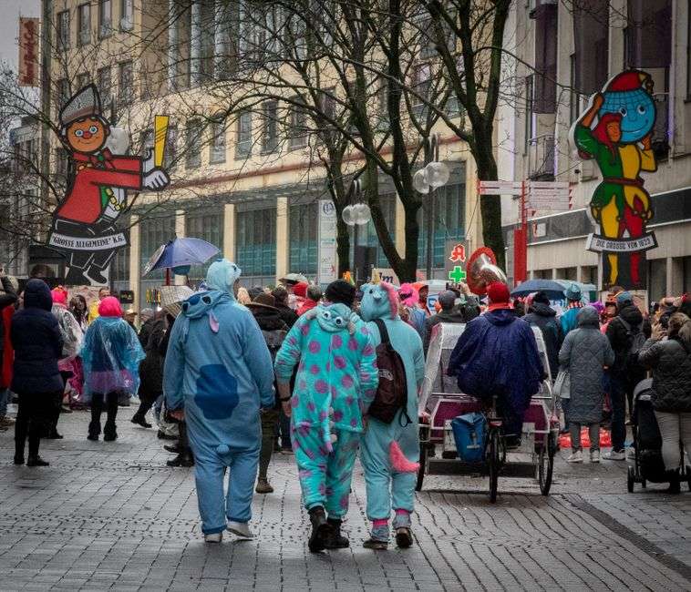 A crowd of parade-goers lines a downtown street watching a Mardi Gras parade go by