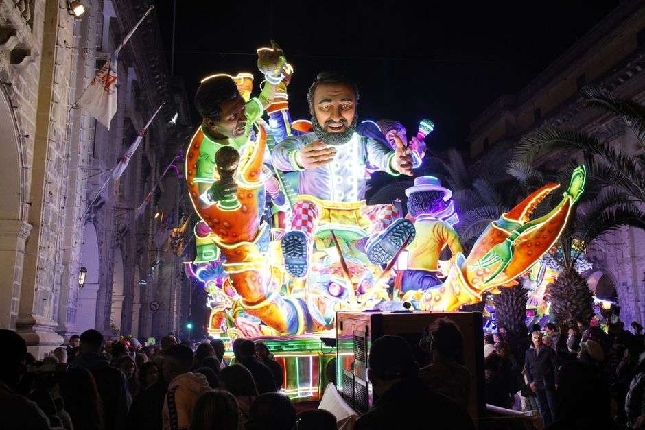A brightly lit Mardi Gras parade float draws a crowd along a nighttime parade route