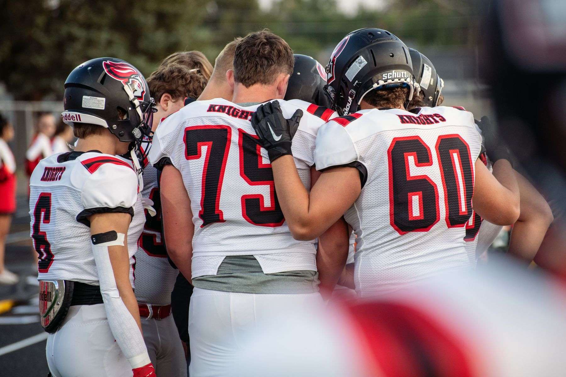 A high school football team gathers in a huddle on the field