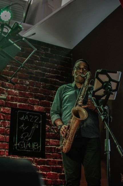 A saxophonist performing under stage lights in a dim jazz club, representing the small but devoted jazz scene in Mobile, Alabama
