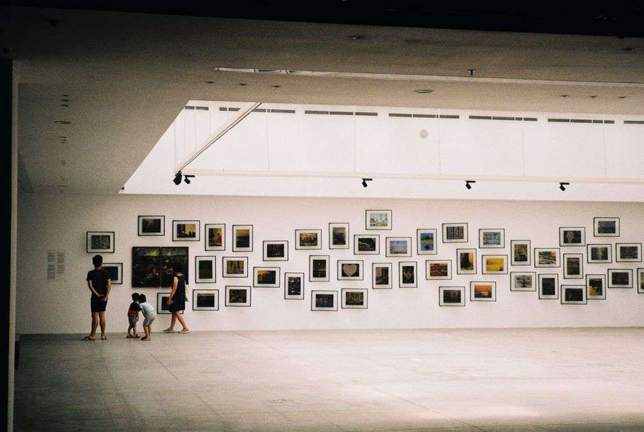 Visitors browse framed artwork on display inside a contemporary art gallery