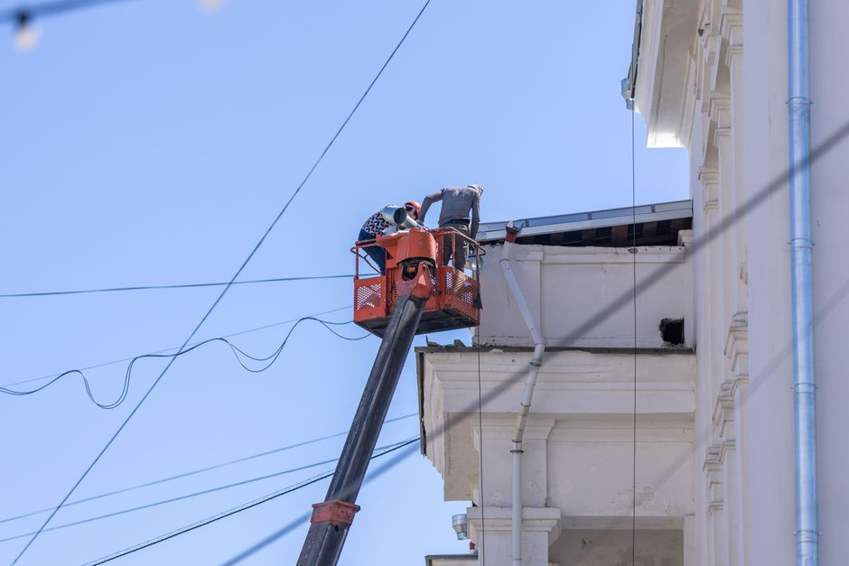 Workers in a crane basket repairing lights on a historic cathedral dome