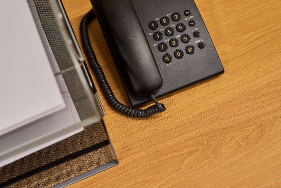 A landline telephone sits on an office desk next to paperwork, representing a monthly phone bill