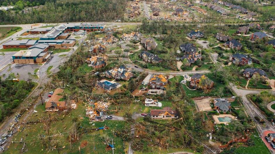 Storm-damaged buildings with a collapsed roof and downed trees after a tornado