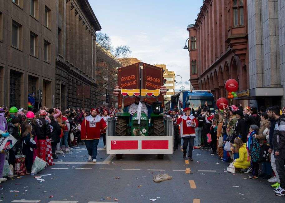 A large crowd lines a downtown street during a Mardi Gras parade as a colorful float passes by