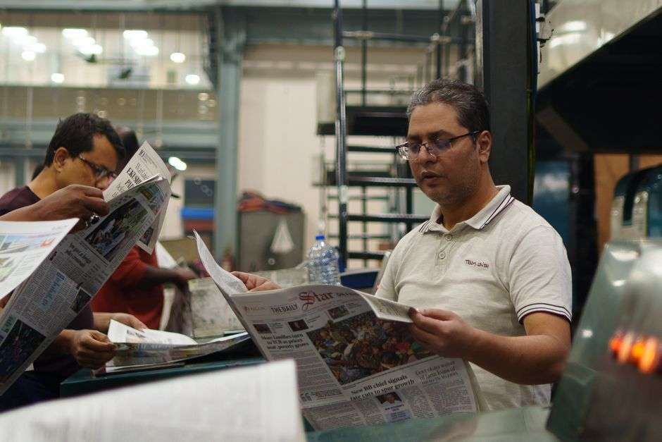 Workers examine freshly printed newspapers at an industrial printing press, representing the end of print publishing for a historic Mobile newspaper