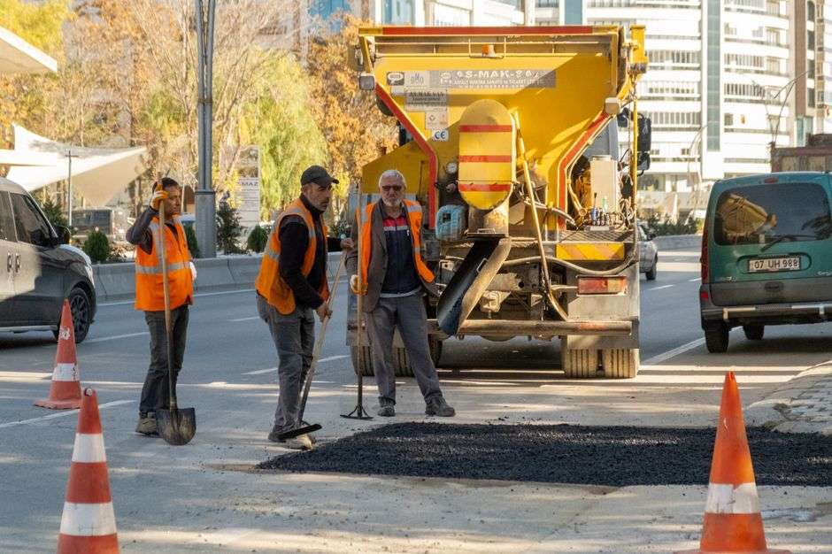A city public works crew in high-visibility vests works on a street with heavy equipment