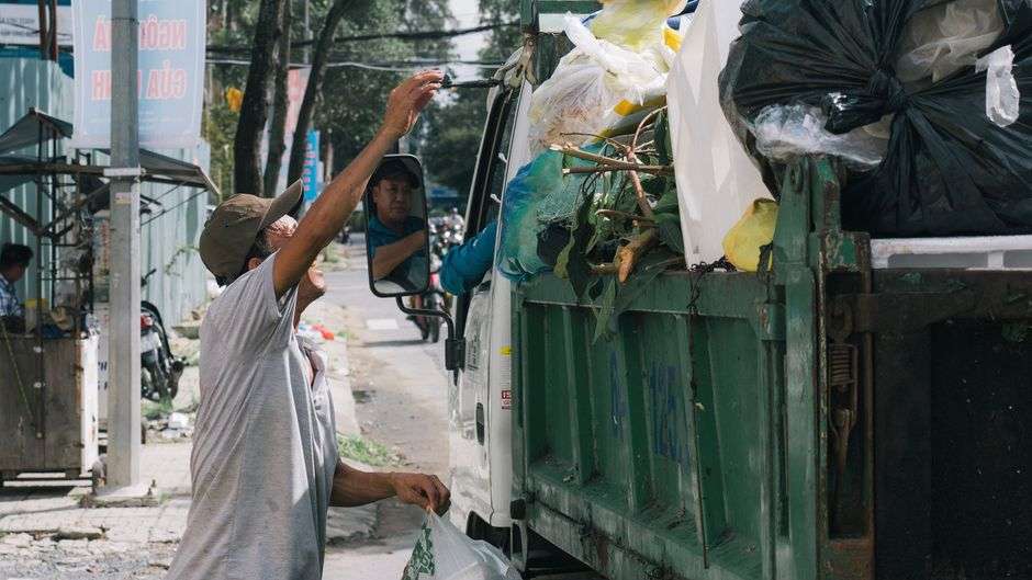 A sanitation worker collects trash along a city street as part of a public works crew