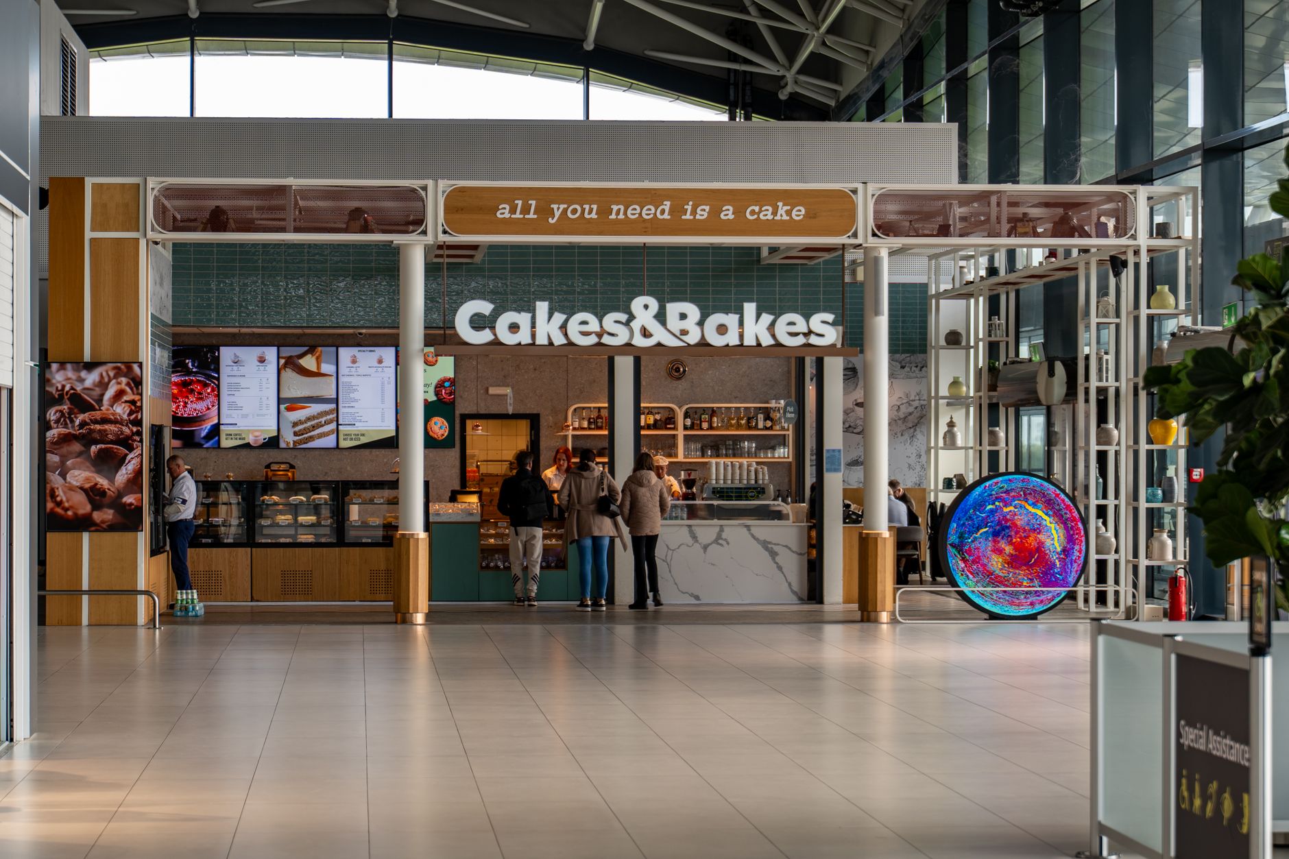 An airport terminal concourse with a newsstand and cafe serving travelers