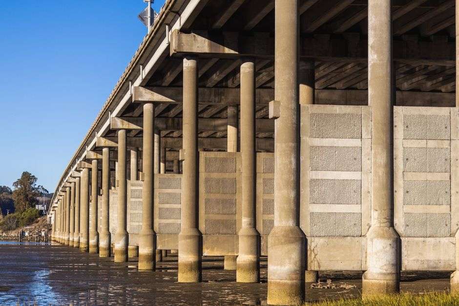 Concrete bridge pillars rising along a riverbank during construction