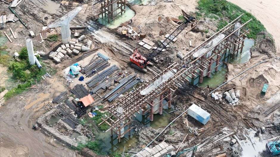 Aerial view of a bridge construction site with pilings and heavy equipment near the water