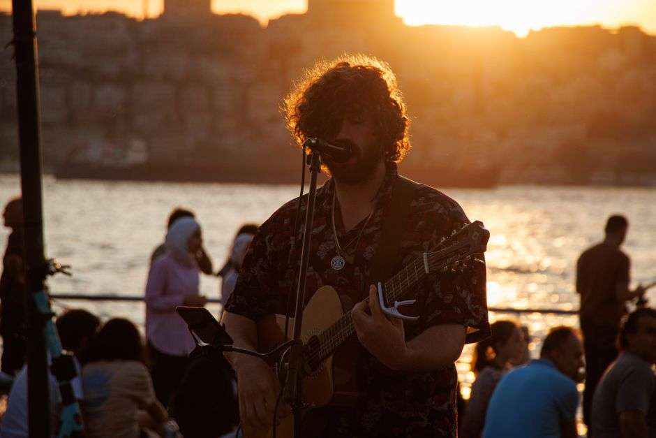 Musician playing acoustic guitar and singing at a waterfront venue at sunset