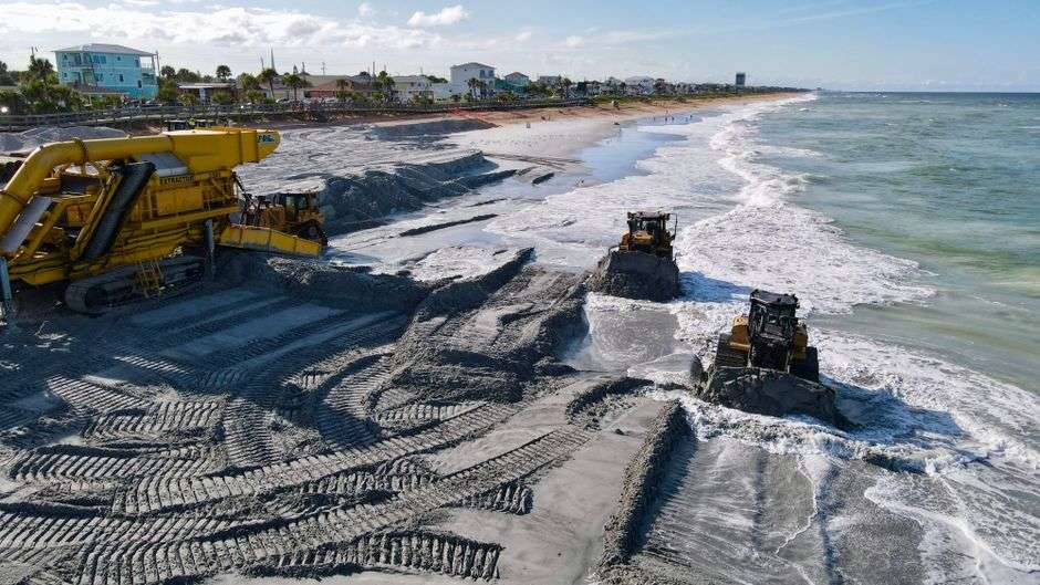 Heavy equipment spreads sand along a beach during a coastal renourishment project