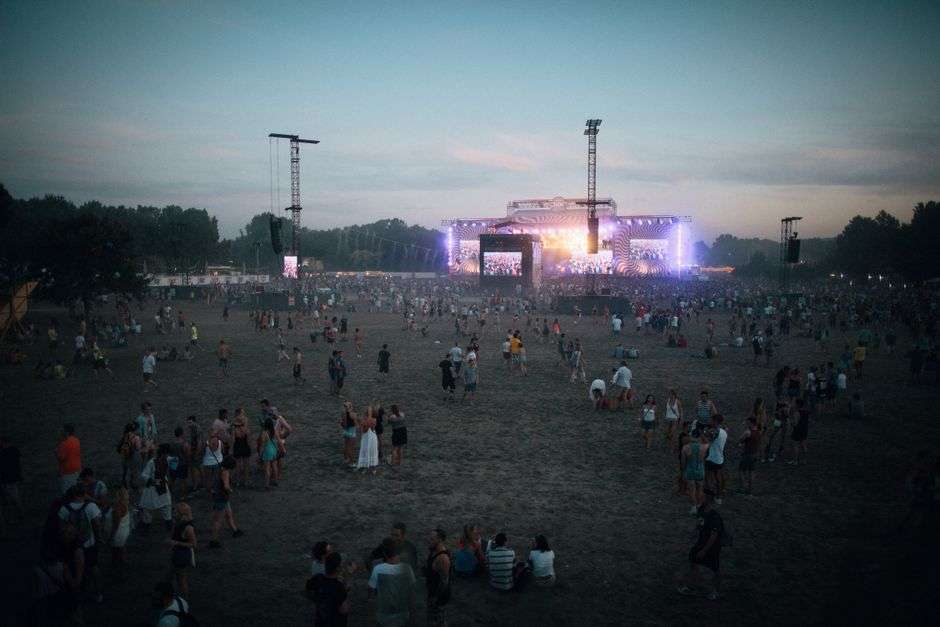 A large crowd gathers on an open field for an outdoor music festival
