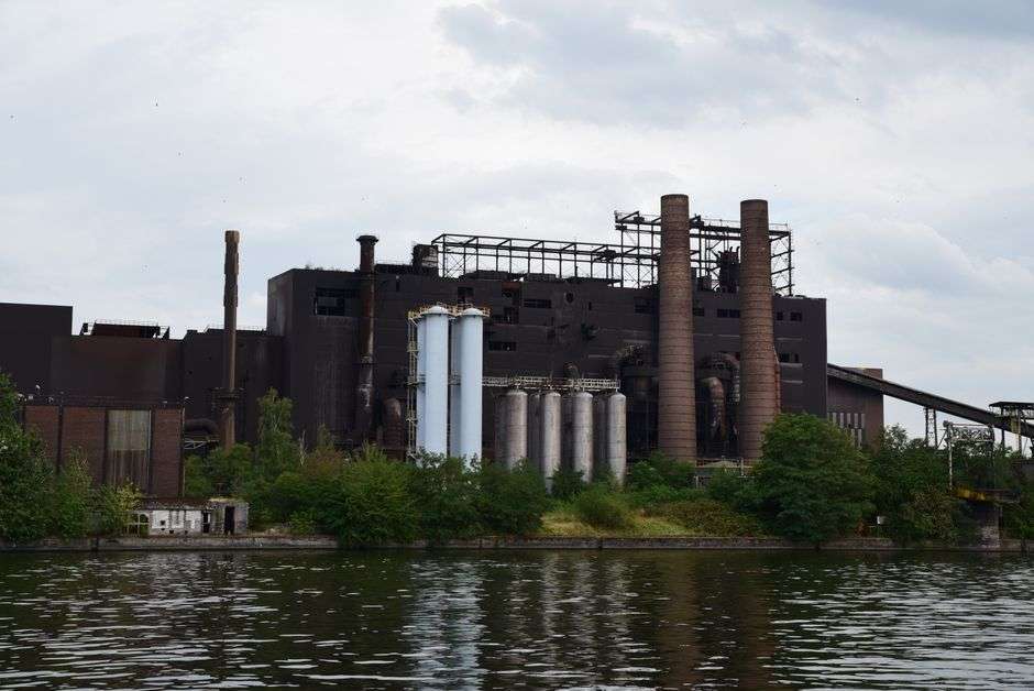 Industrial power plant buildings along a river bank surrounded by trees