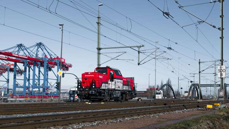 Freight rail cars and cranes at a port terminal where cargo trains share tracks with other rail traffic