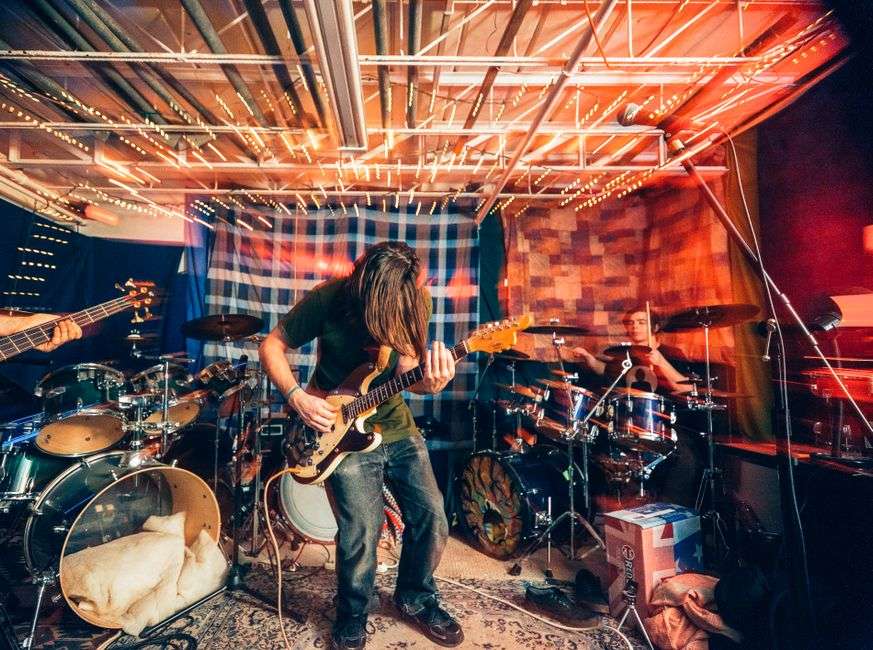 A band performs live on stage with electric guitar and drums under colorful stage lights