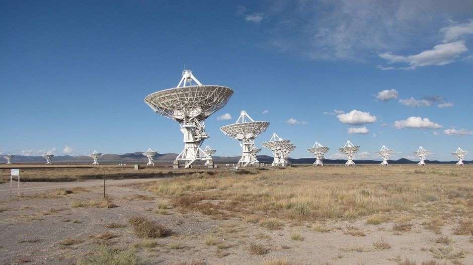 A cluster of large radio telescope dishes under a clear sky, used for scanning space for signals