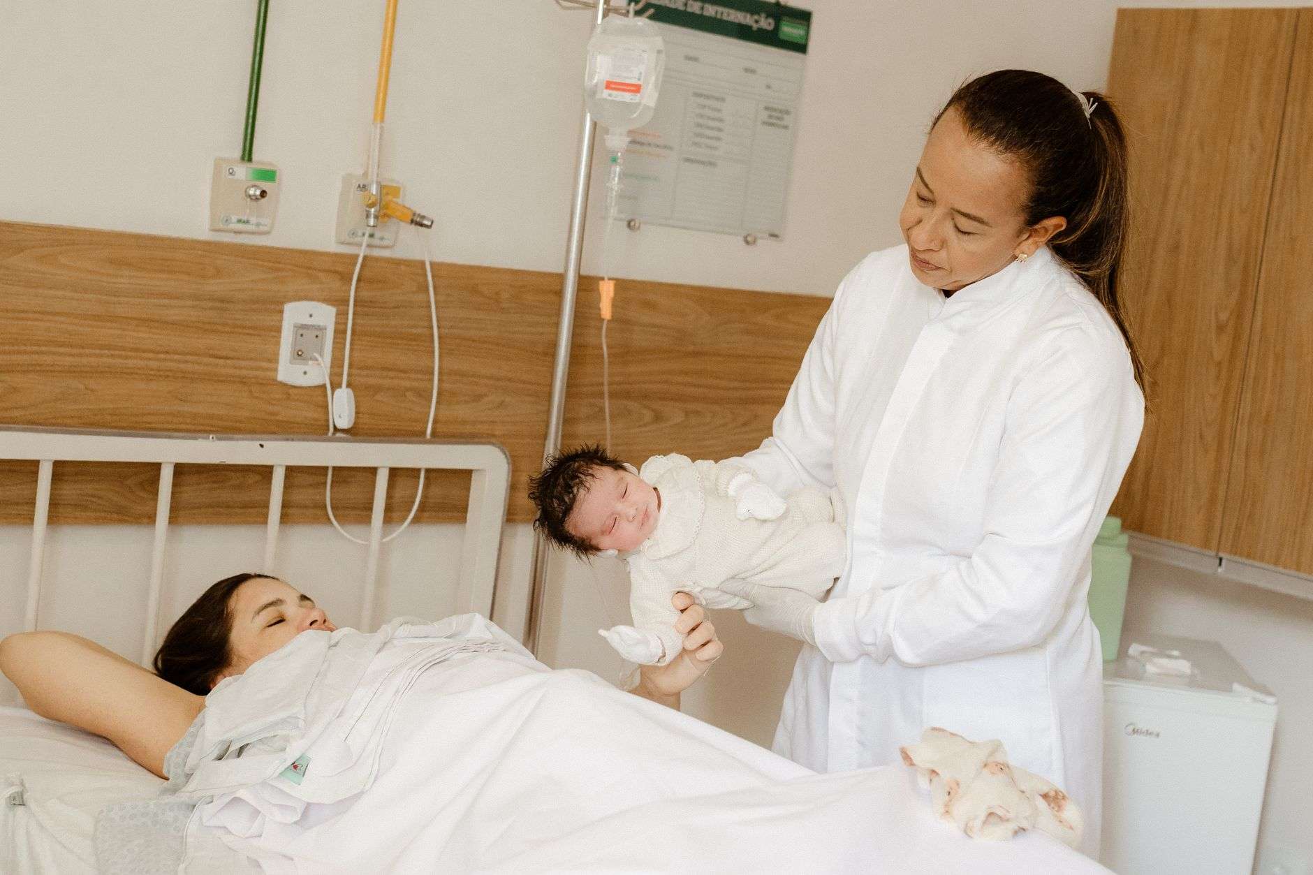 A doctor assists a new mother with her newborn baby in a hospital maternity ward