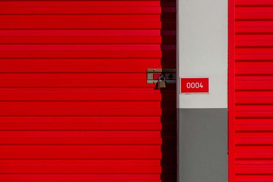 A red metal self-storage unit door secured with a padlock