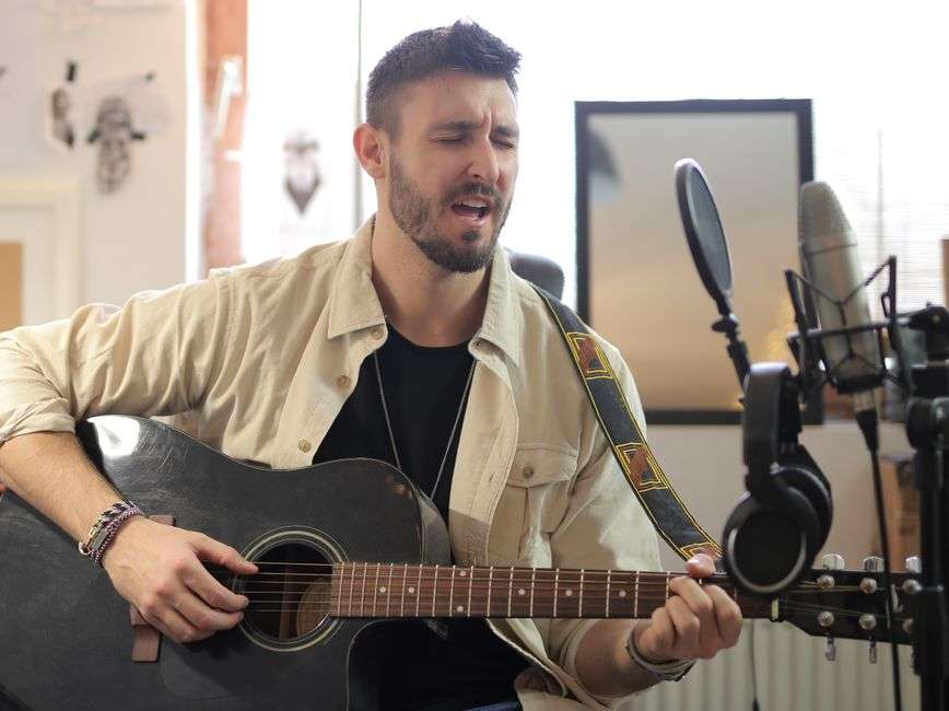 A singer-songwriter plays acoustic guitar while recording vocals in a music studio