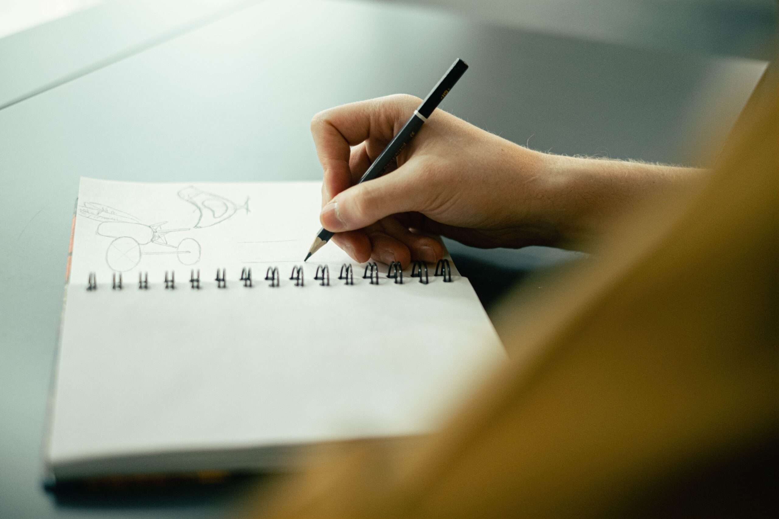 A close-up of a hand sketching with a pencil in a spiral notebook, evoking a casual drawing meetup