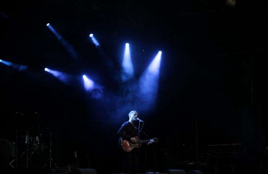 A songwriter performs on stage with an acoustic guitar during an evening concert