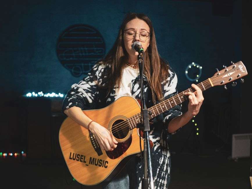 A female singer-songwriter performs live with an acoustic guitar and microphone