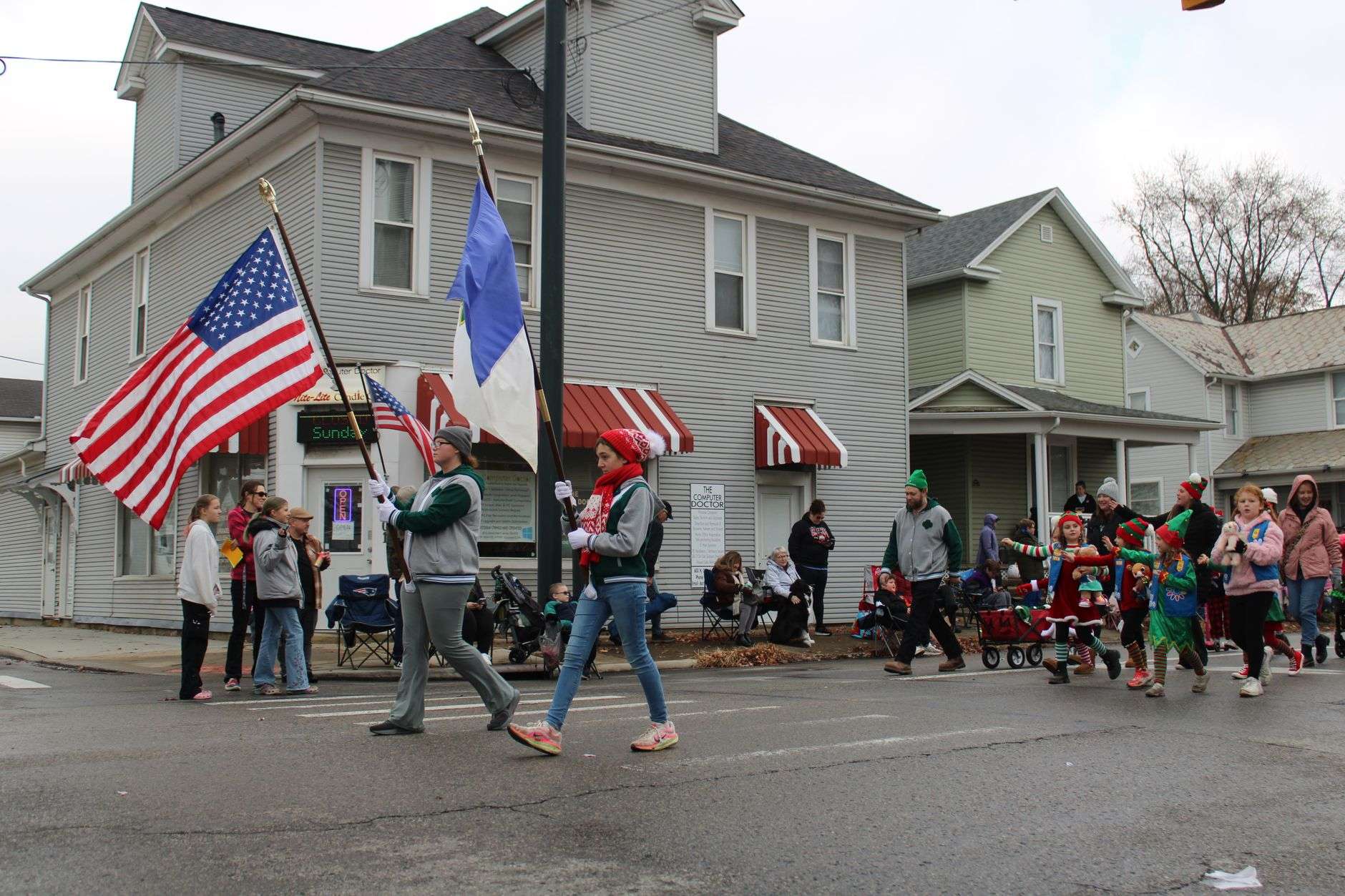 A community parade with participants carrying flags down a small-town street