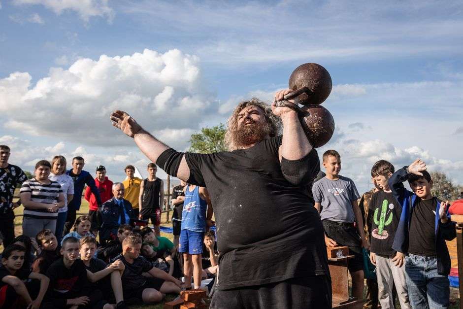 Strongman competitor lifting a heavy weight outdoors during a strength competition as a crowd watches
