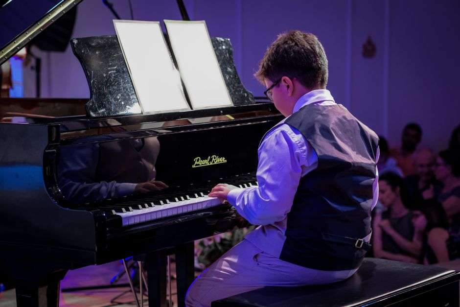 A young student performs on a grand piano during a music competition recital