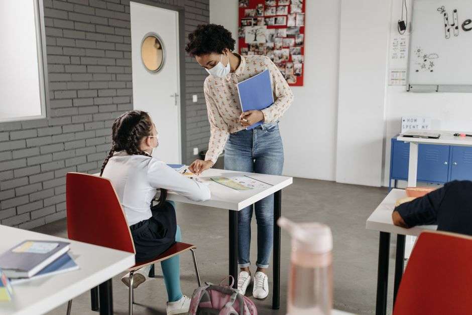 Teacher wearing a face mask helps a student at a desk in a classroom