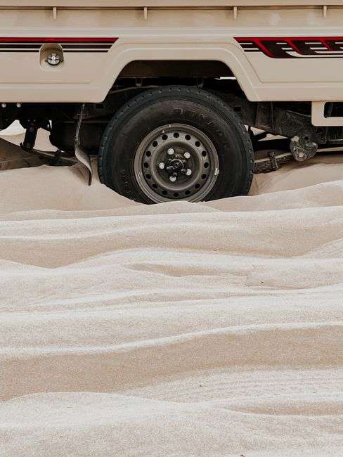 Close-up of a vehicle tire buried deep in loose sand, illustrating the kind of sand buildup that can trap vehicles near the coast