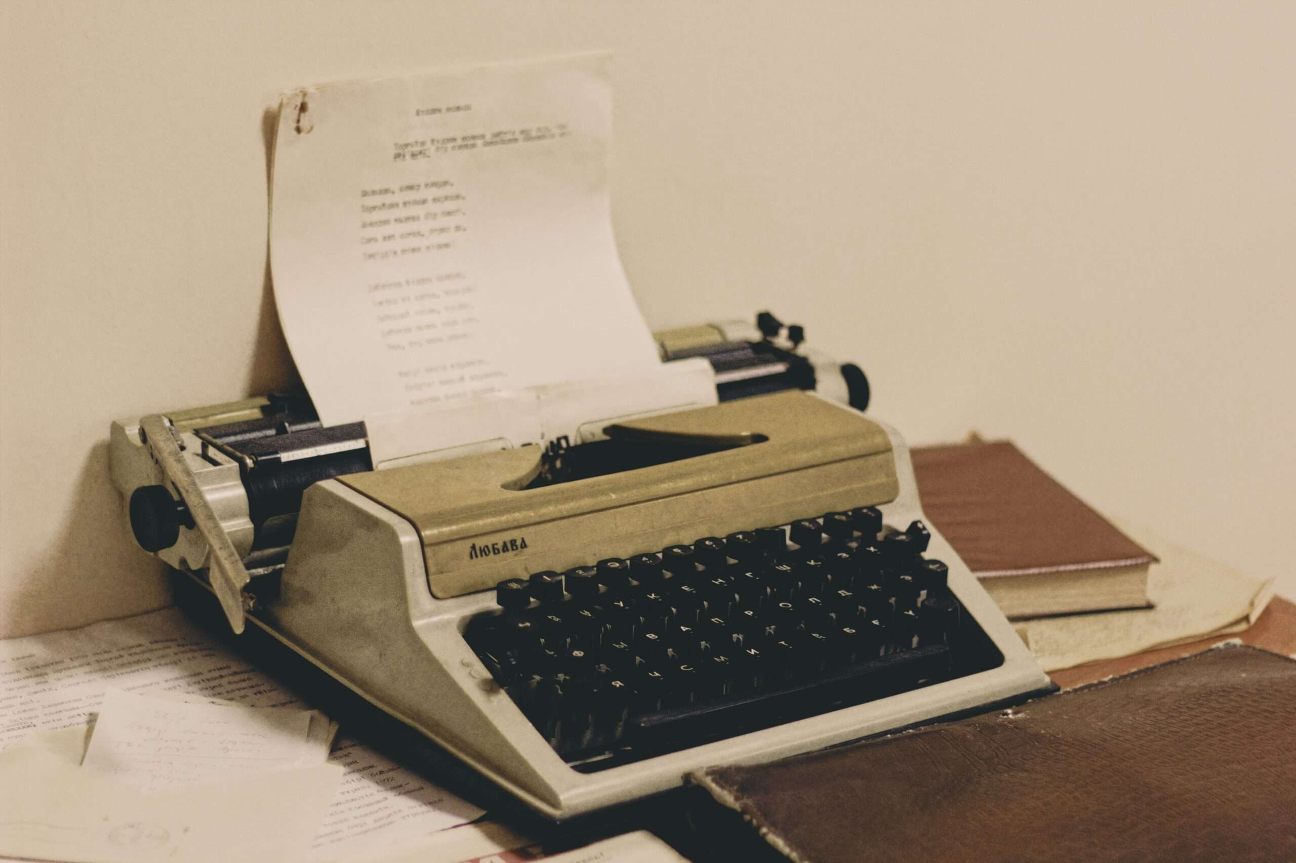 A vintage typewriter sits on a desk surrounded by stacks of books