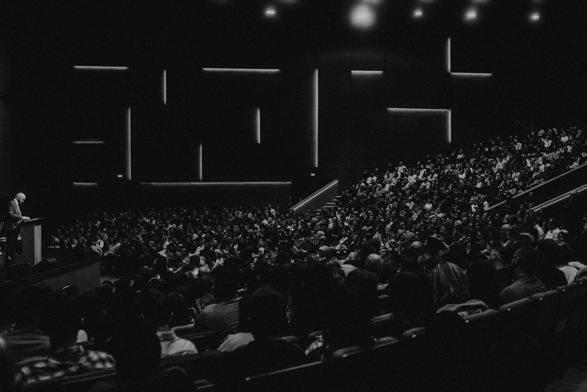 Speakers seated on a panel before an audience in a meeting hall