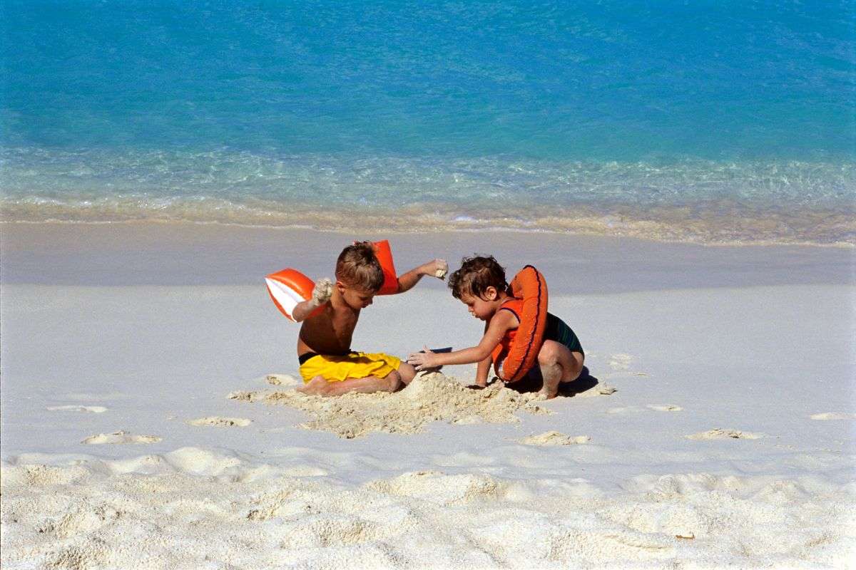 Two children wearing life jackets play in the sand at the beach