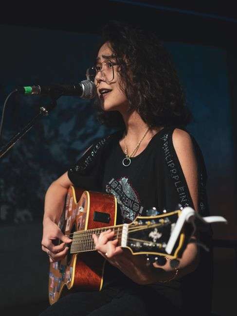 A singer-songwriter performing solo with an acoustic guitar under stage lights
