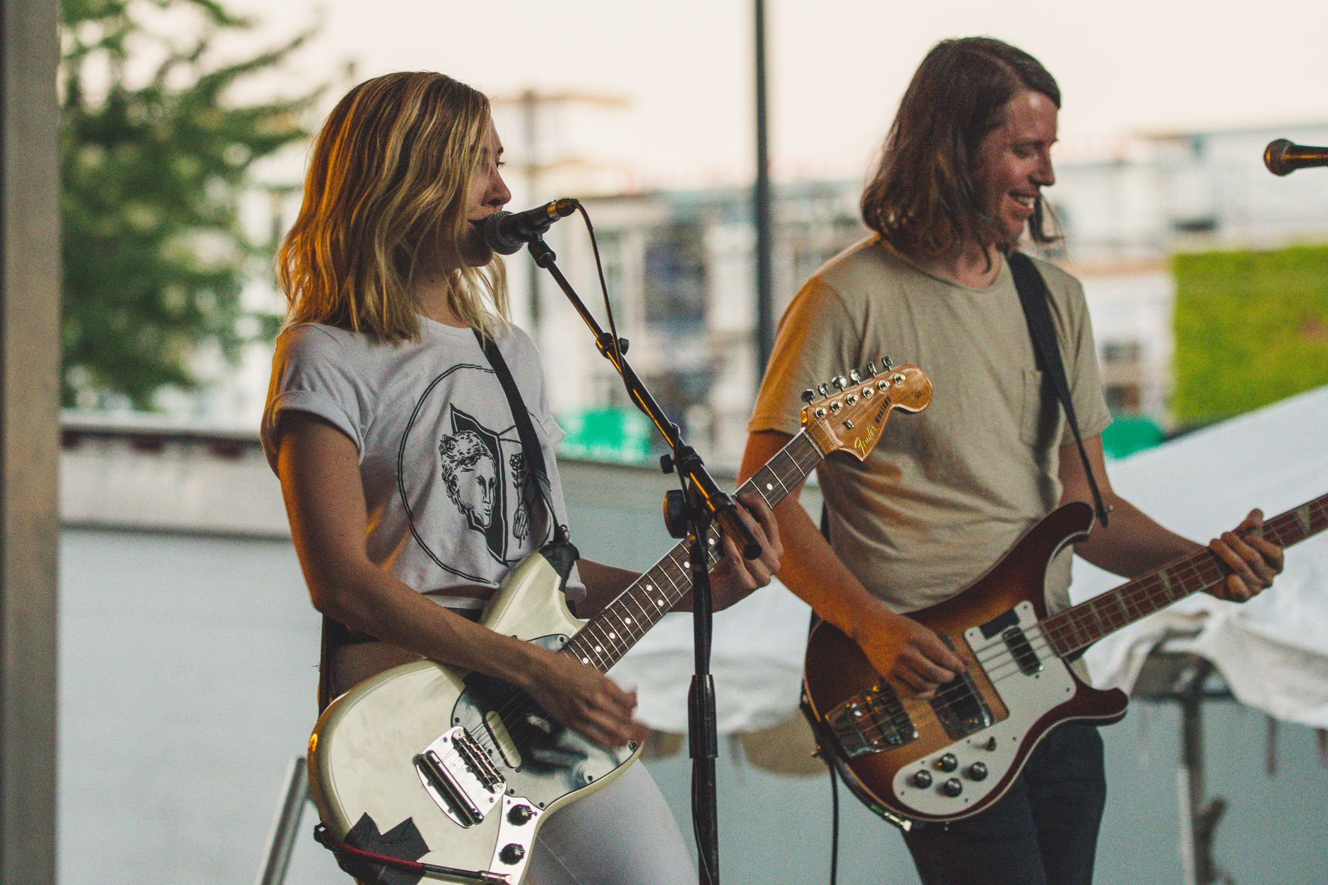 A man and woman perform live on stage, singing and playing guitars together outdoors.