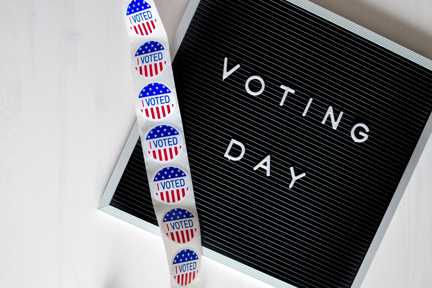 A strip of red, white, and blue "I Voted" stickers next to a black felt letter board spelling out "VOTING DAY"