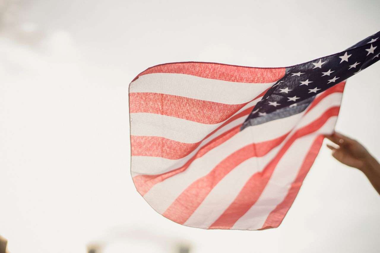 A person holding an American flag against the sky
