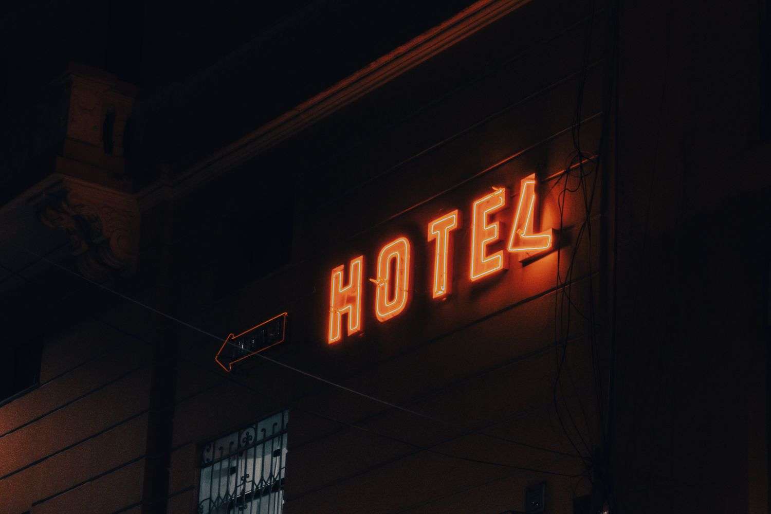 Illuminated red neon HOTEL sign glowing on a building exterior at night, with an arrow sign below it