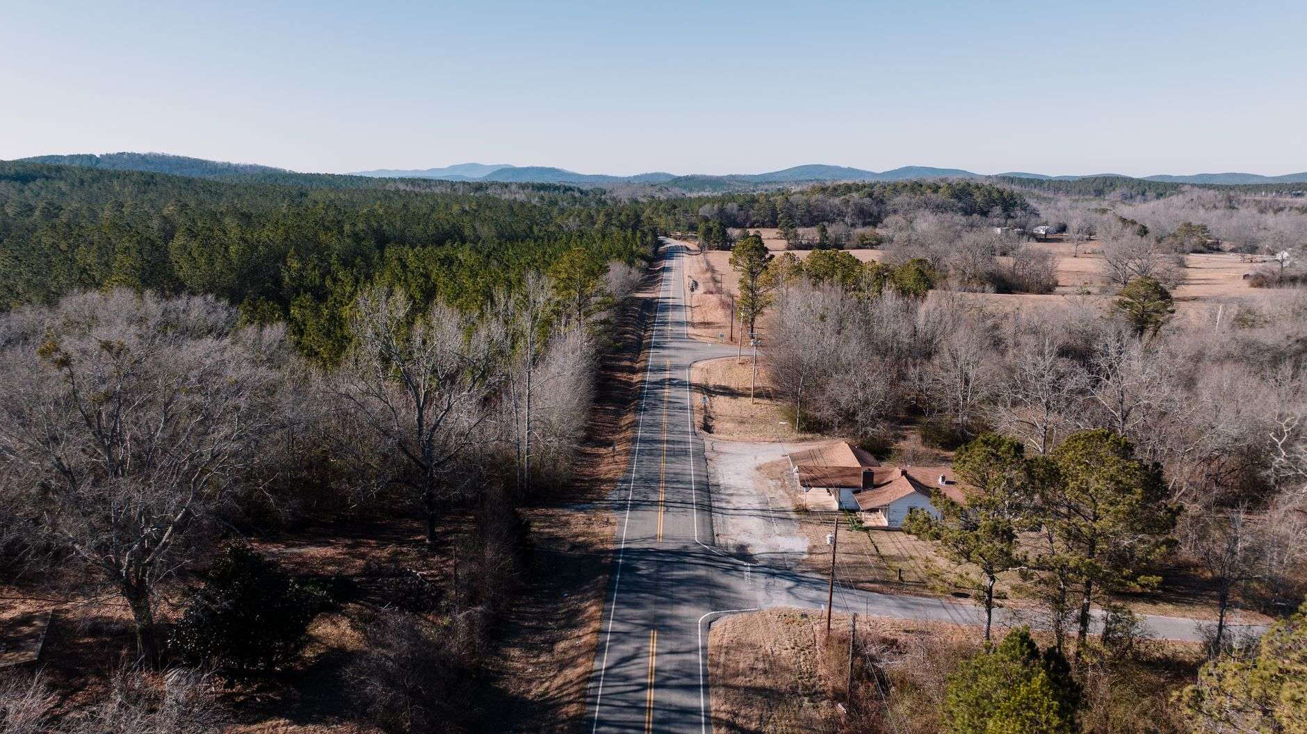A rural two-lane Alabama road surrounded by trees under a clear sky