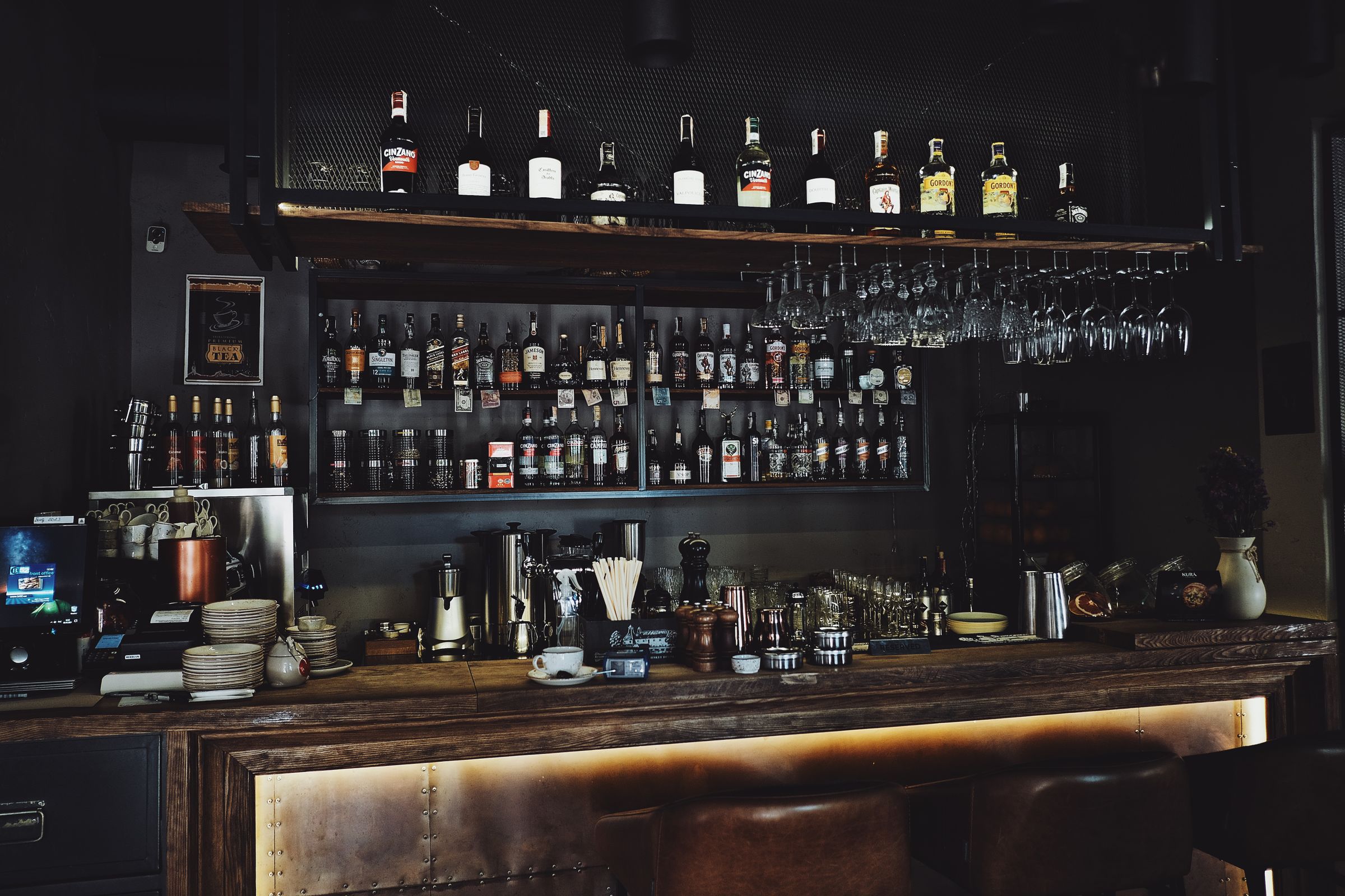 Bar shelf lined with bottles of liquor and hanging wine glasses above a wooden counter