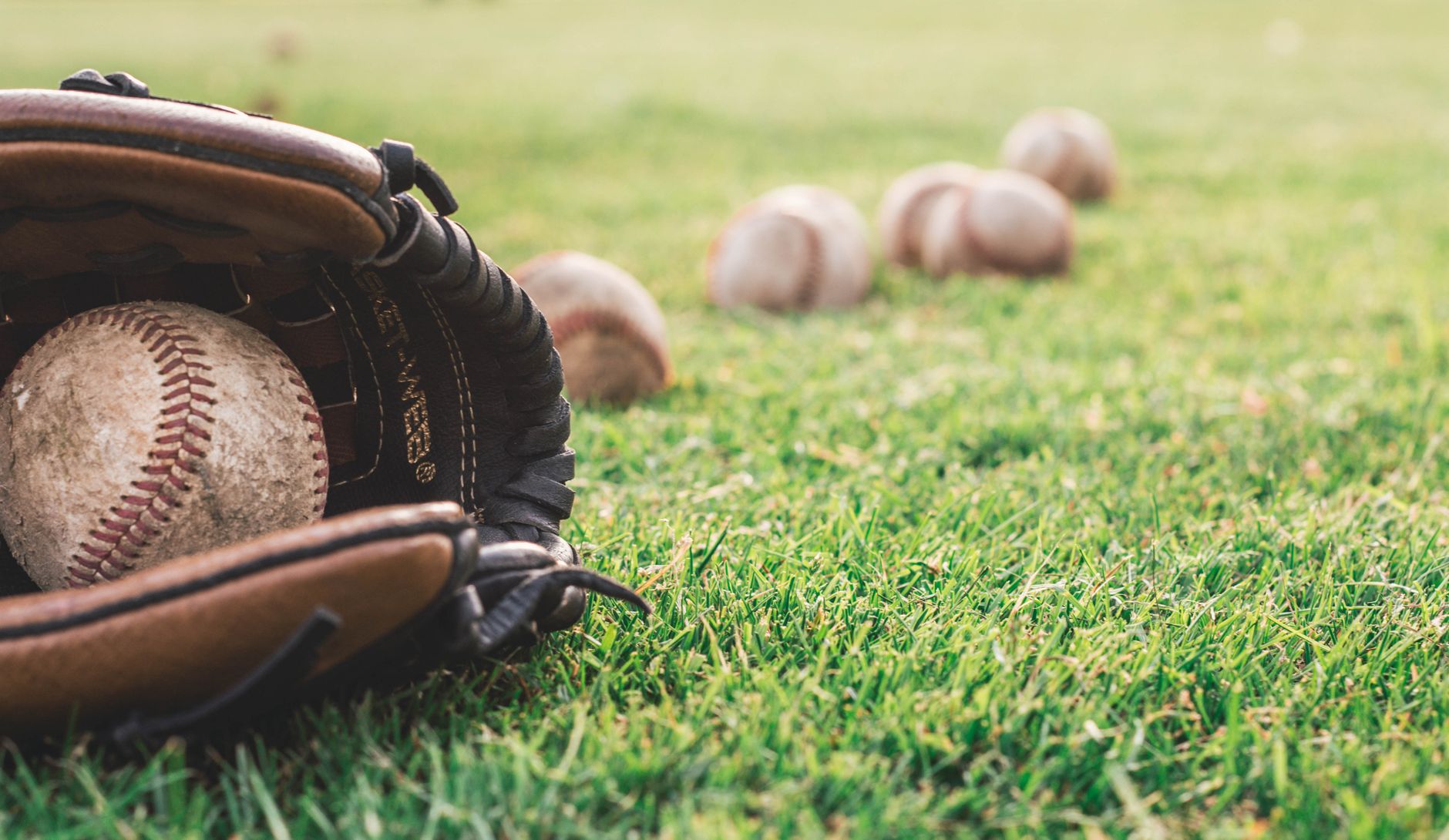 Close-up of a leather baseball glove holding a baseball, with several more baseballs on a grass field