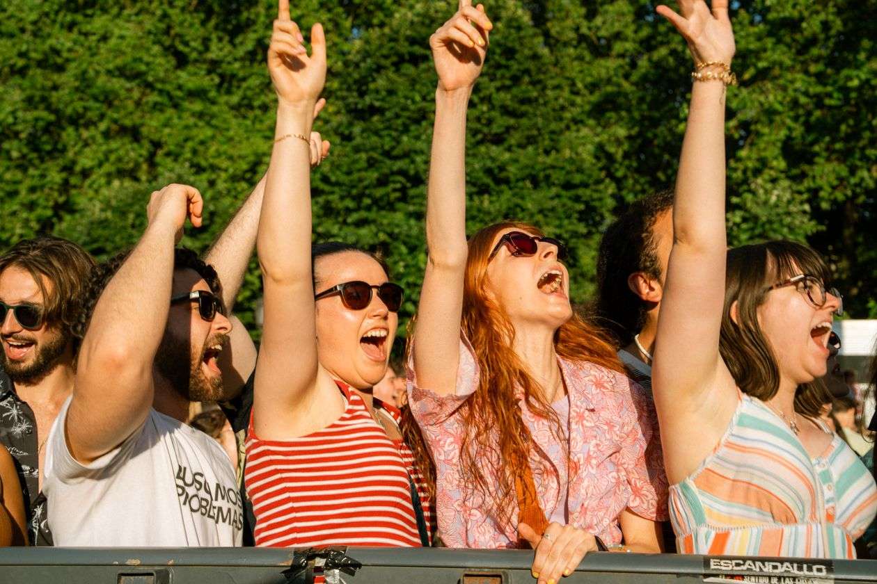 A crowd cheering with hands raised at an outdoor summer music festival, similar to BayFest in Mobile