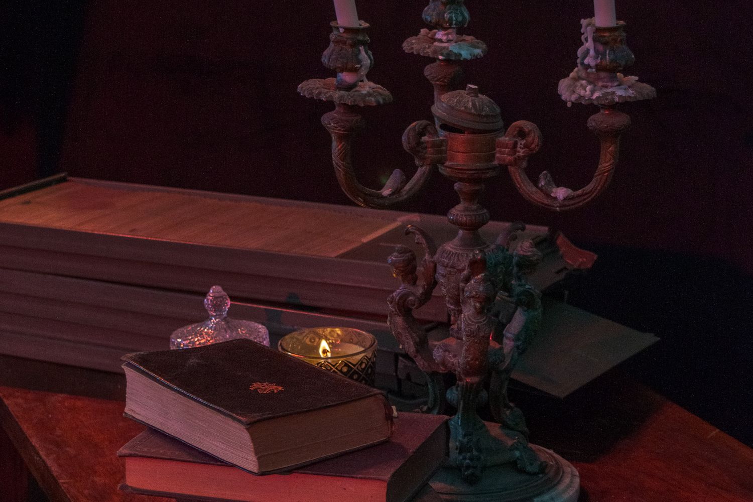 A candlelit home altar with antique books and ritual objects in a darkened room