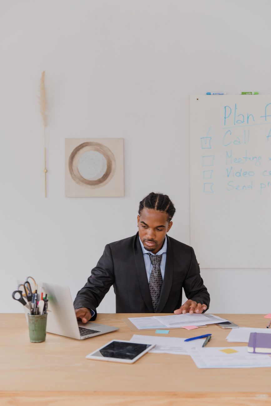 Man in a suit reviewing paperwork and using a laptop at a desk