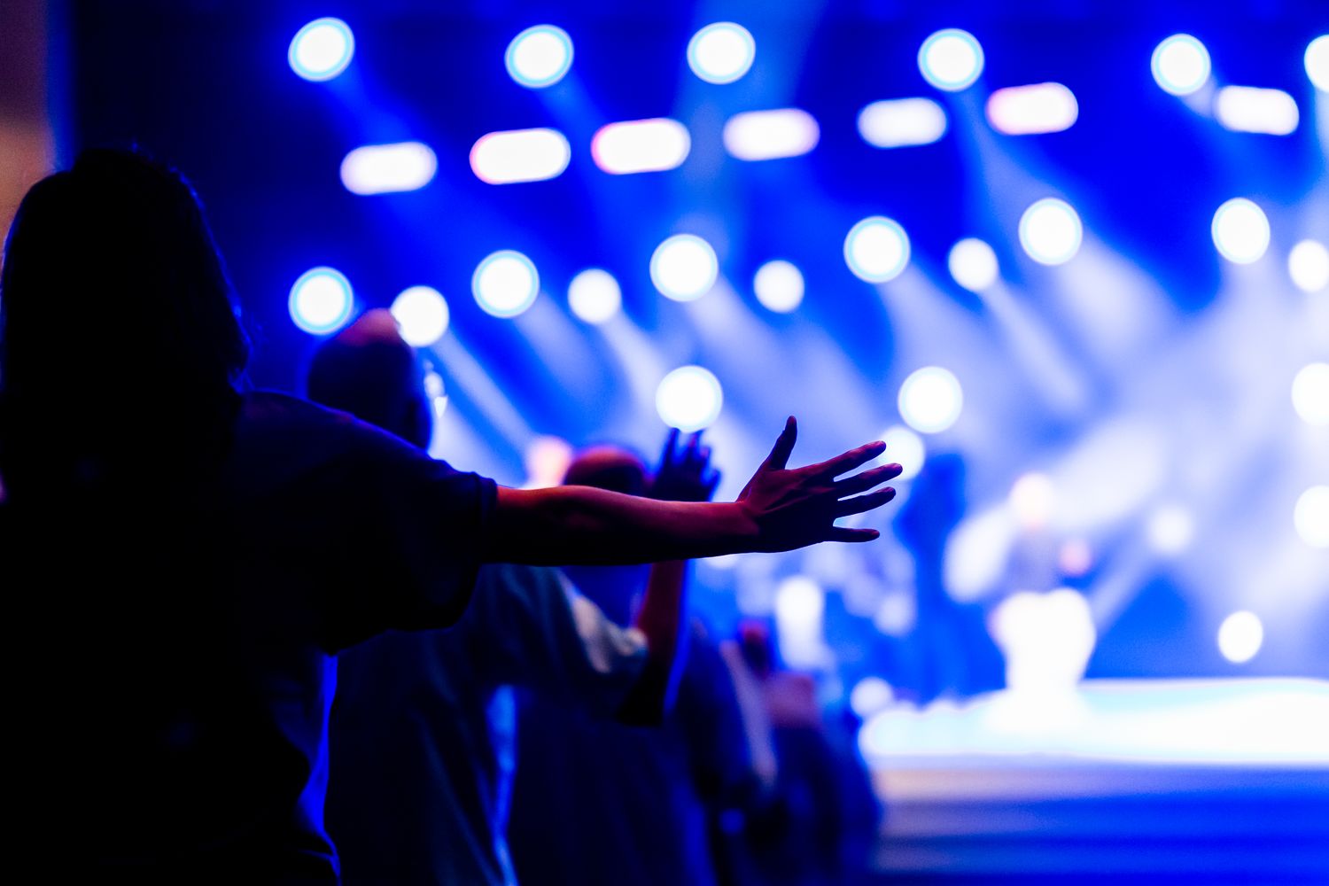 Audience with raised hands beneath bright stage lighting at a live concert