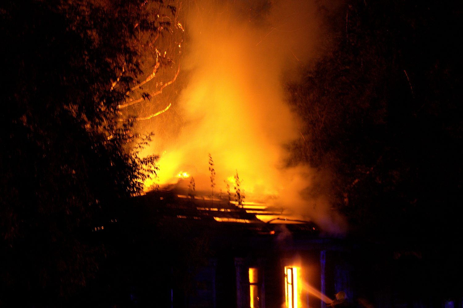 Flames rise from the back of a residential home as firefighters respond
